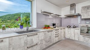 A modern kitchen with a large window, stainless steel appliances, and a view of a green landscape. - Villa Over the Hilltop by Interhome (Motovun)