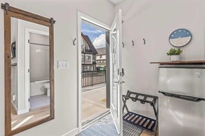 Un pasillo con un espejo, una puerta que da a un balcón, un reloj y un refrigerador.