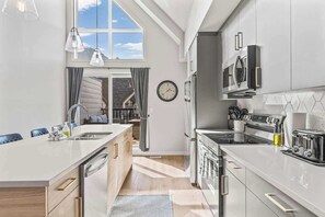 A modern kitchen with a central island, stainless steel appliances, and a large window.
