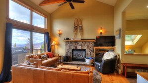 A cozy living room with a stone fireplace, leather sofas, and a large window overlooking a deck.