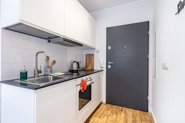 A compact kitchen with a black countertop, stainless steel sink, and a black door.