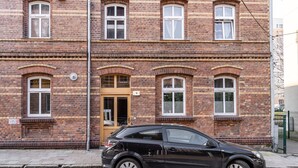 A black car parked in front of a brick building with multiple windows and a door marked with the number 9. - Janasa Comfort Studio (Katowice)