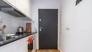 A compact kitchen with white cabinets, a black door, and a wooden floor. - Janasa Comfort Studio (Katowice)
