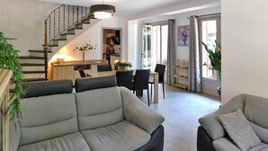 A modern living room with a grey sofa, a dining area with a table and chairs, and a staircase leading to an upper floor. - Les Hauts De Sarlat La Caneda (SARLAT LA CANEDA)