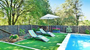A backyard with a swimming pool, two lounge chairs, a small garden area with flowers, and a wooden fence. - Les Hauts De Sarlat La Caneda (SARLAT LA CANEDA)