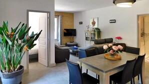 A modern living room with a dining area, a TV, and a plant. - Les Hauts De Sarlat La Caneda (SARLAT LA CANEDA)