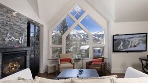 Amplia sala de estar con chimenea, ventanas grandes que ofrecen vistas a la montaña y un televisor de pantalla plana montado en la pared.