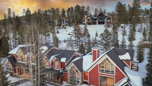 Un gran lodge de varios pisos con fachada roja y amplias ventanas, rodeado de árboles cubiertos de nieve y un paisaje montañoso.