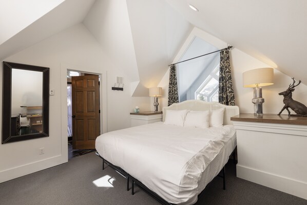 A bedroom with a large bed, a nightstand, a lamp, a mirror, and a deer sculpture.