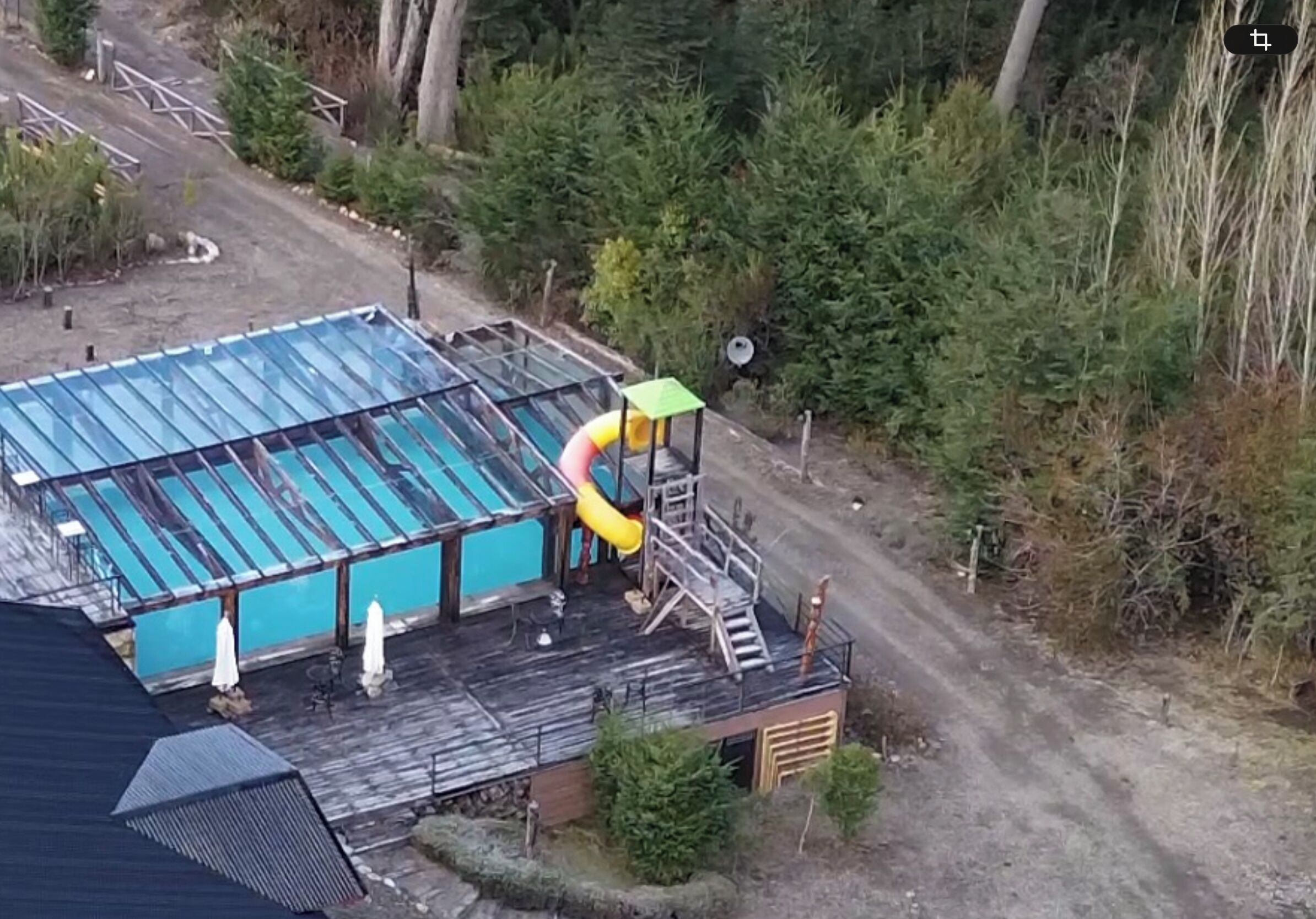 Piscina com escorregador, cercada por árvores e um deck de madeira.