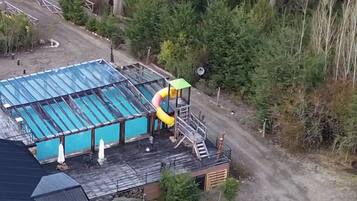 Piscina com escorregador, cercada por árvores e um deck de madeira.