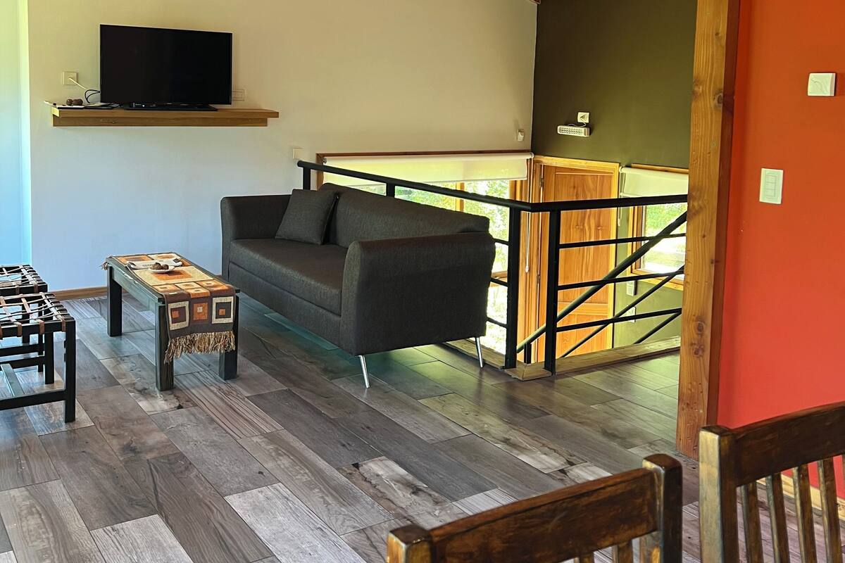 A cozy living room with a wooden ceiling, a sofa, a coffee table, and a TV on a shelf.