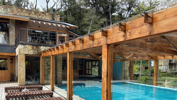 Ein moderner Poolbereich im Freien mit Holzliegen und einem Steinhaus im Hintergrund.