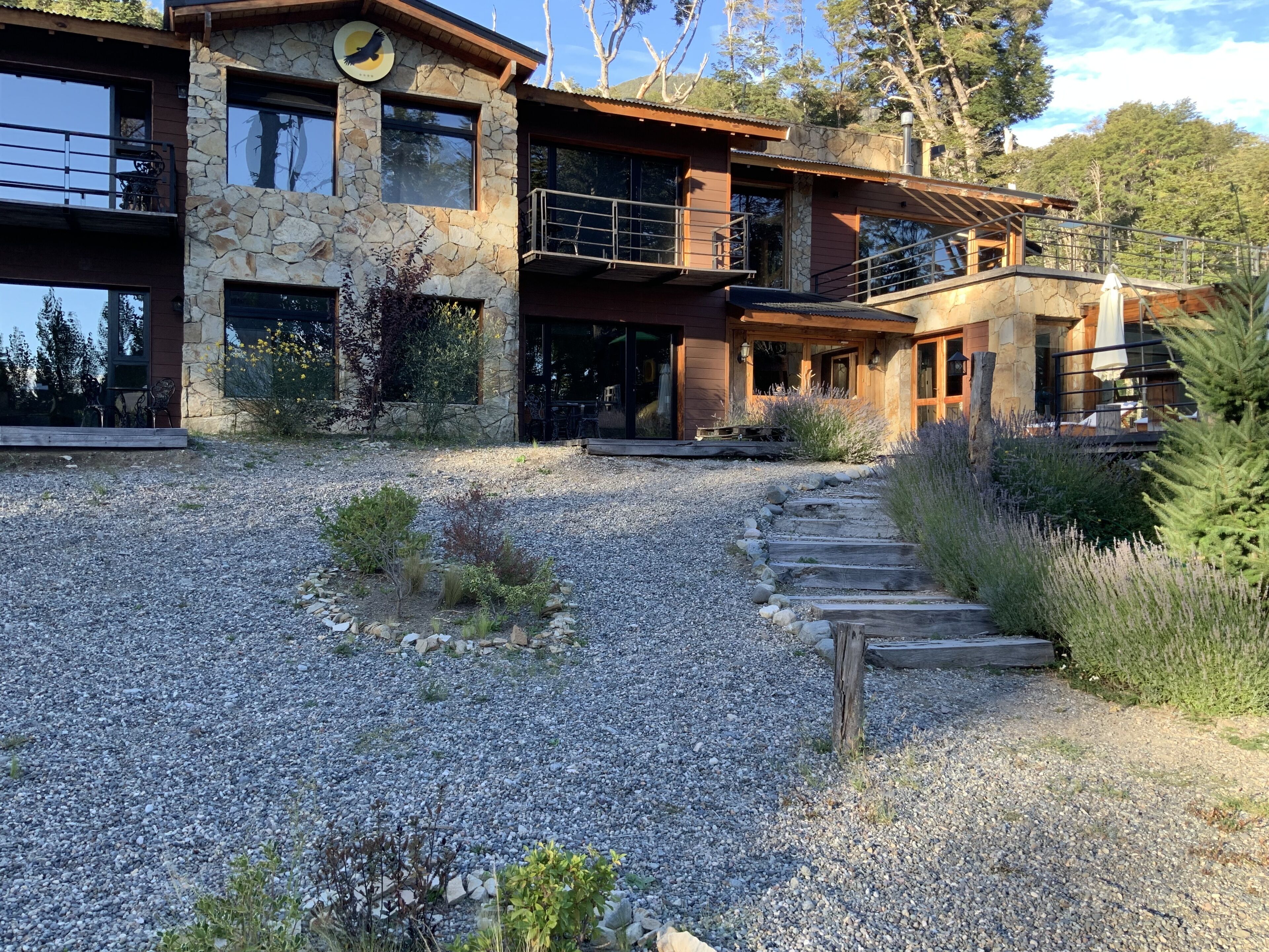 A modern two-story house with a stone facade, a balcony, and a gravel driveway leading to the entrance.