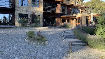 A modern two-story house with a stone facade, a balcony, and a gravel driveway leading to the entrance.
