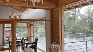 Ein Holzinterieur mit einer Chandelüster, großen Fenstern und einem Essbereich mit Stühlen und einem Tisch.