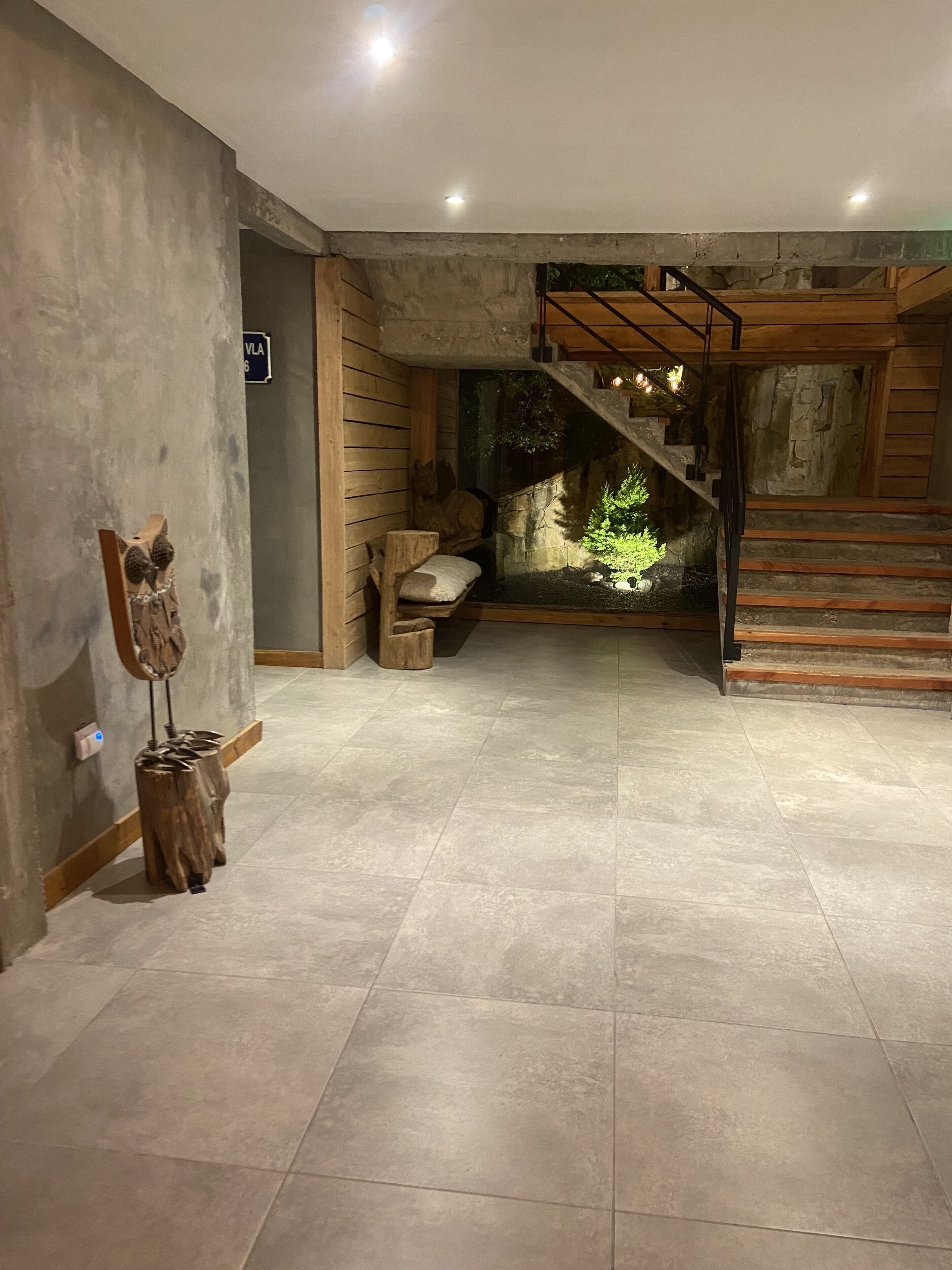 Un amplio pasillo con pared de piedra, una escalera de madera y un pequeño jardín interior.