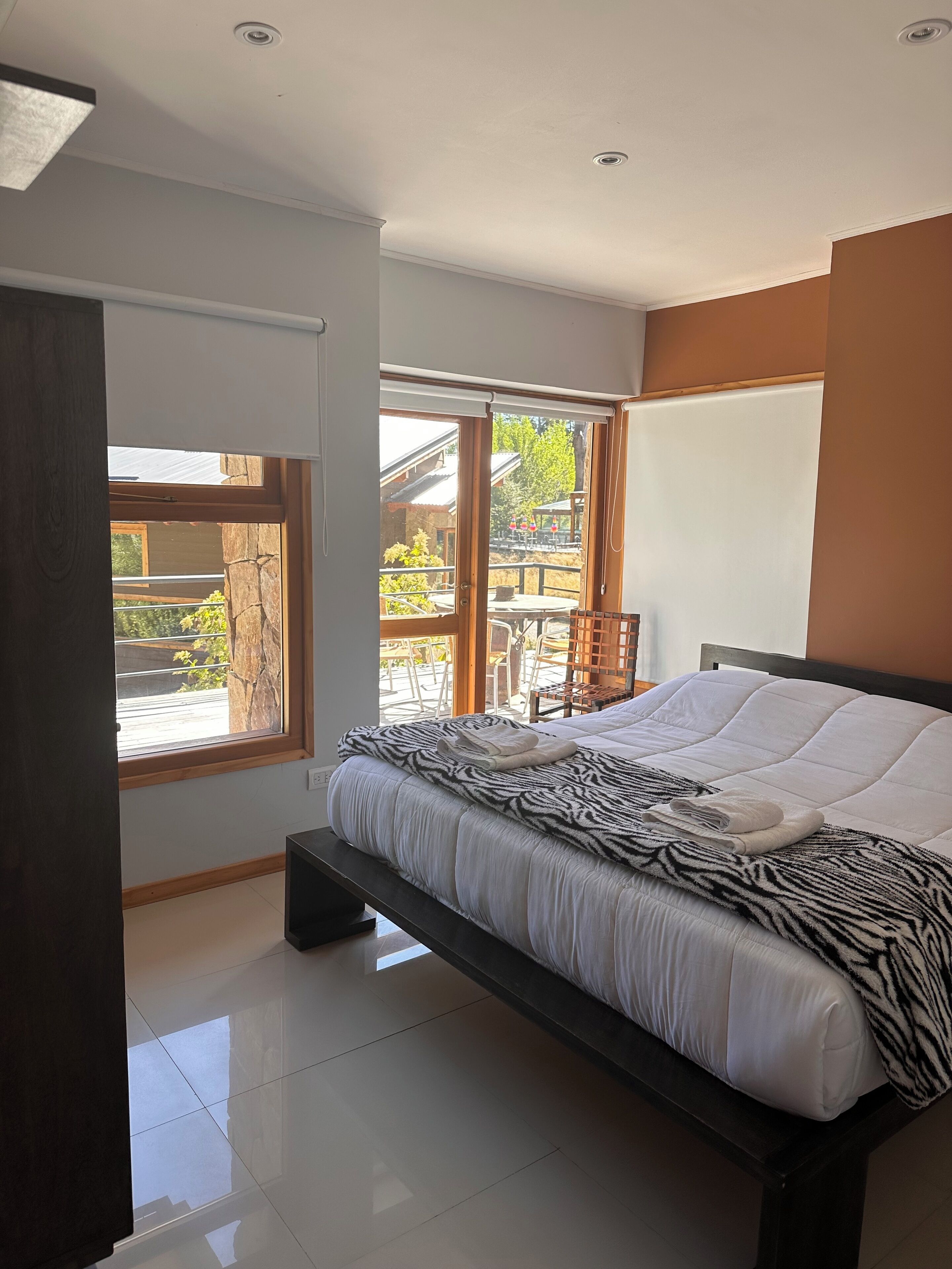 Un dormitorio moderno con una cama grande, un banco y vistas a un patio exterior con mesas y sillas.