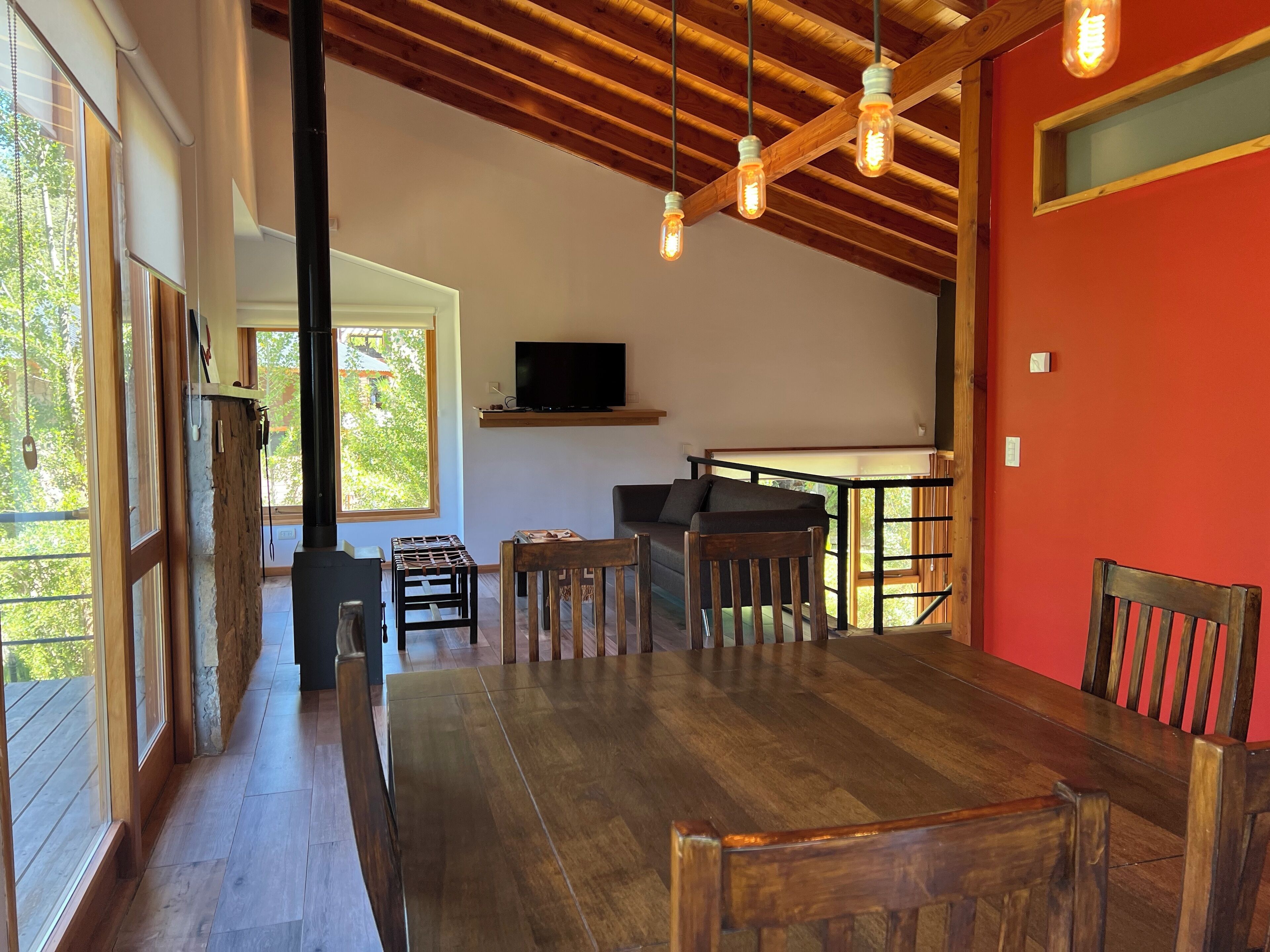 Amplia sala de estar con mesa de comedor de madera, un sofá y un televisor montado en la pared.
