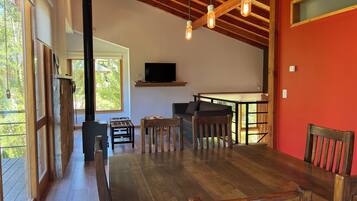 Amplia sala de estar con mesa de comedor de madera, un sofá y un televisor montado en la pared.