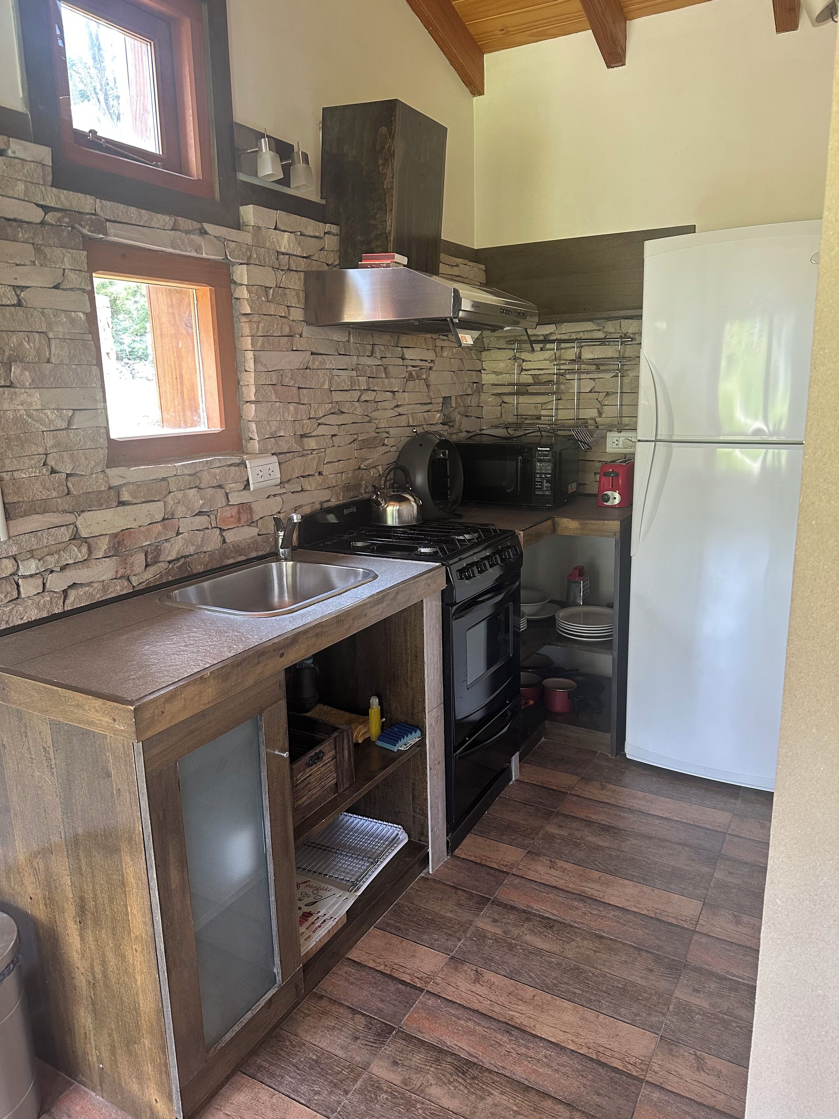 A kitchen with a stone wall, a gas stove, a microwave, and a white refrigerator.