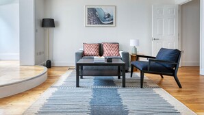 A modern living room with a sofa, armchair, coffee table, and a painting on the wall.