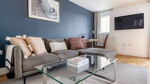 Un salon moderne avec un canapé gris, une table basse en verre et un téléviseur fixé au mur.