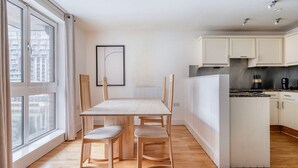 Une cuisine moderne avec des meubles blancs, une table à manger avec des chaises et une vue sur la ville grâce à de grandes fenêtres.