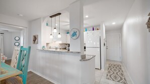 Une cuisine moderne avec des meubles blancs, un plan de travail en granit, des luminaires suspendus et une décoration murale représentant une tortue.