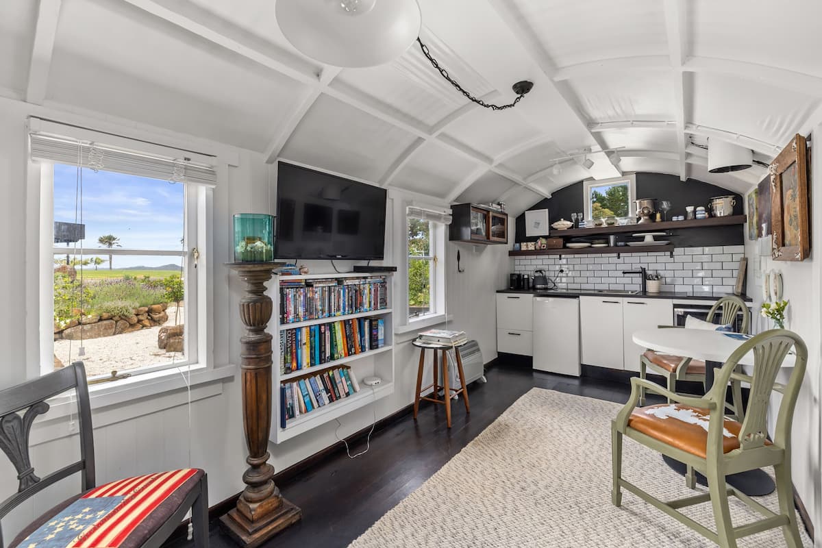 A spacious kitchen with white cabinets, a large window, and a bookshelf filled with books.