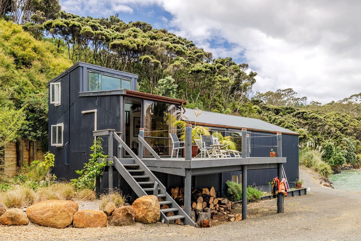 A modern house with a balcony overlooking a river, surrounded by lush greenery.