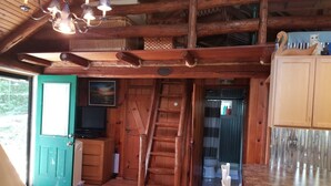 Interior rústico de una cabaña con una escalera de madera, un comedor y una cocina con mostrador de metal.