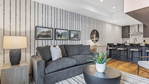 Un salon moderne avec un canapé gris, une table basse ronde agrémentée d’une plante et un papier peint à rayures.