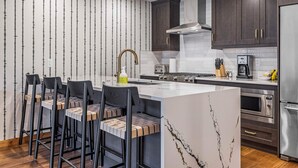 Une cuisine moderne dotée d’un îlot central, de tabourets de bar, de meubles en bois foncé, d’appareils électroménagers en acier inoxydable et d’un crédence décorée.