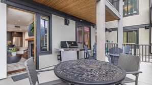 Une terrasse extérieure avec une table ronde et des chaises, un barbecue et une vue sur l’intérieur.