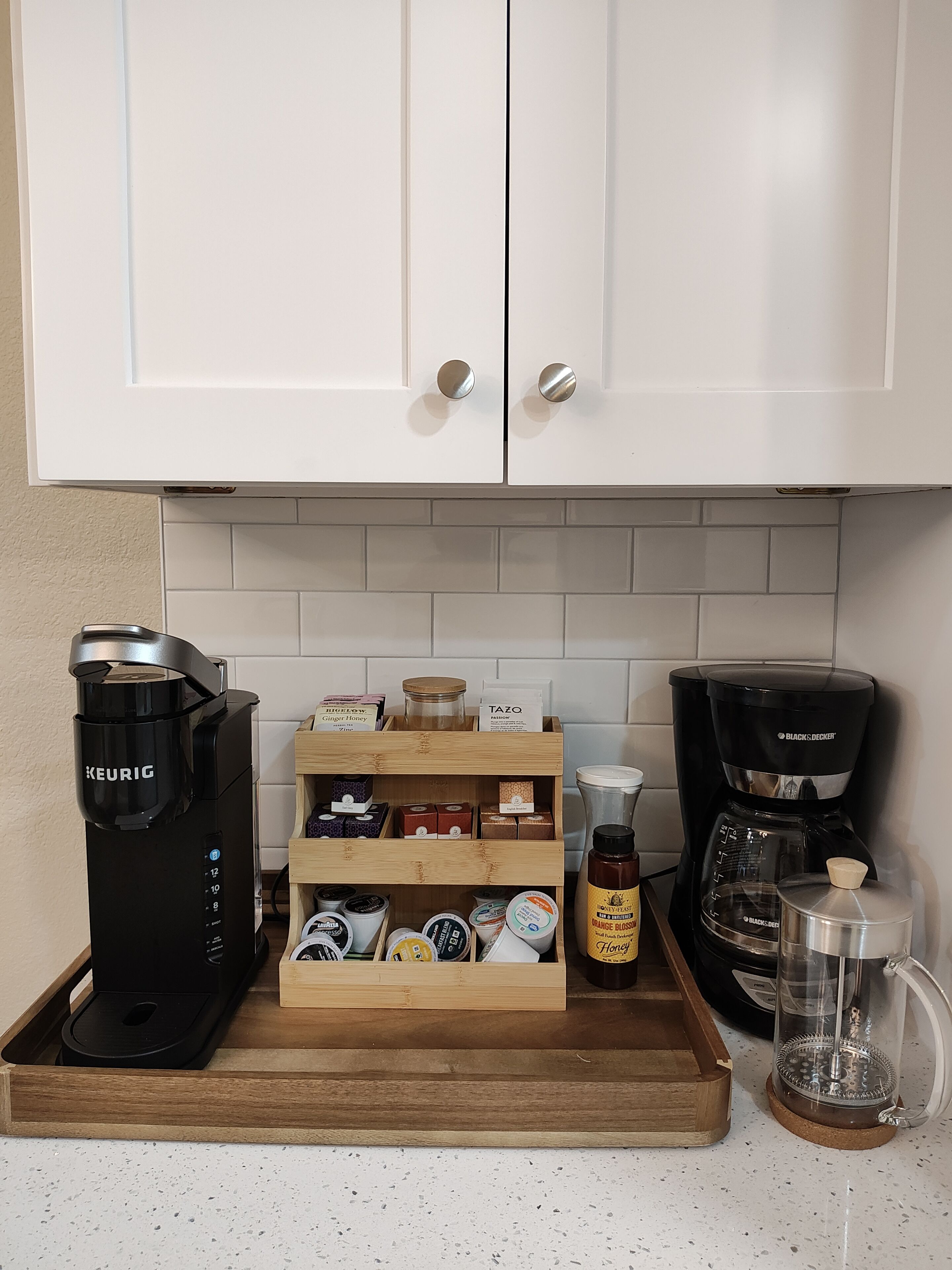 A kitchen with white cabinets, a wooden spice rack, a Keurig coffee maker, a Black & Decker coffee maker, and a glass carafe.