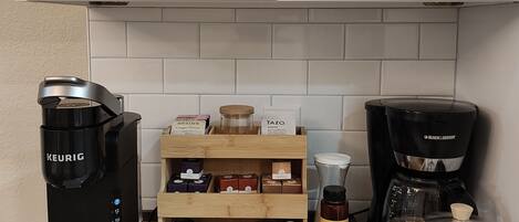 A kitchen with white cabinets, a wooden spice rack, a Keurig coffee maker, a Black & Decker coffee maker, and a glass carafe.
