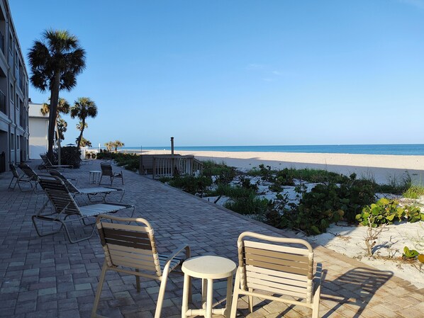 A beachside patio with lounge chairs and a table, overlooking the beach and ocean.