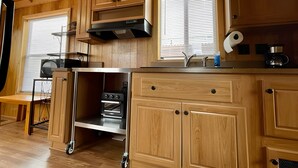 A compact kitchen with wooden cabinets, a built-in oven, a microwave, and a window with blinds. - Cozy cabin in delightful Kemmerer with AC, WiFi (Kemmerer)