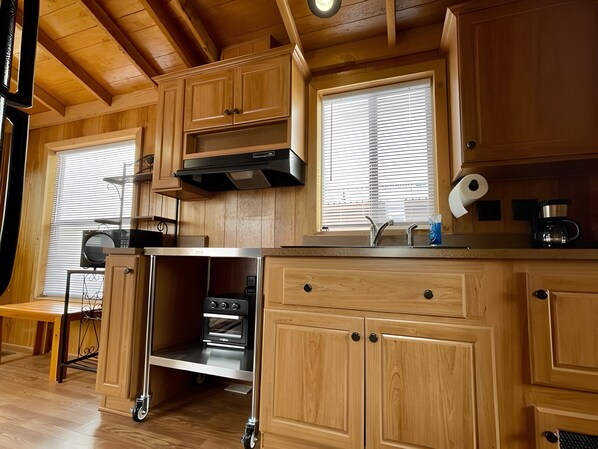 A compact kitchen with wooden cabinets, a built-in oven, a microwave, and a window with blinds. - Cozy cabin in delightful Kemmerer with AC, WiFi (Kemmerer)