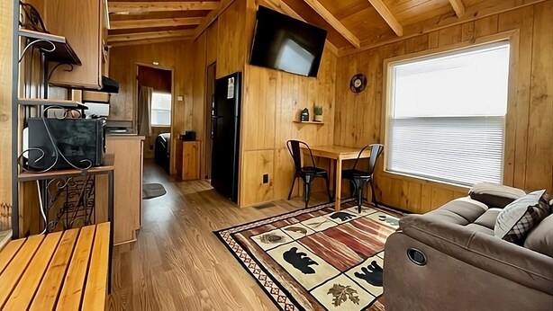 A cabin interior with a wooden interior, a dining area, a sofa, and a TV mounted on the wall. - Cozy cabin in delightful Kemmerer with AC, WiFi (Kemmerer)
