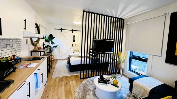 A modern, compact living space with a kitchenette, a bed, a seating area, and a TV. - Stylish tiny home in Melton west (Melton West)