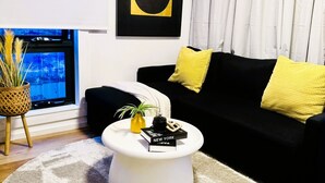 A modern living room with a black sofa, a white coffee table, and a large abstract painting on the wall. - Stylish tiny home in Melton west (Melton West)