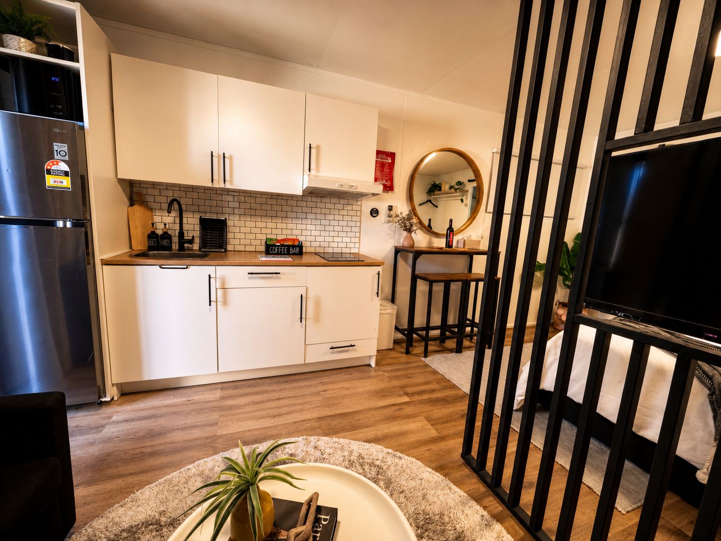 A modern kitchen with white cabinets, a stainless steel refrigerator, a coffee bar, and a round mirror on the wall.