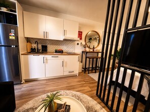 Une cuisine moderne avec des armoires blanches, un réfrigérateur en acier inoxydable, un coin café et un miroir rond accroché au mur.