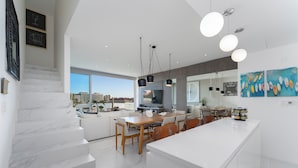 A modern kitchen with a large island, white marble stairs, and a dining area with a view of the city. - Elegant Penthouse with Private Terrace, BBQ & Jacuzzi (Cabo San Lucas)