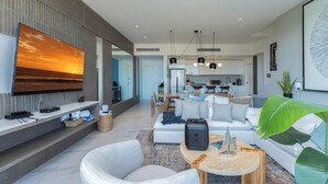 A modern living room with a large TV, a sofa, a coffee table, and a dining area in the background. - Elegant Penthouse with Private Terrace, BBQ & Jacuzzi (Cabo San Lucas)