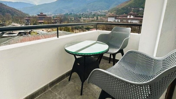 Un balcon avec une table et deux chaises, donnant sur un paysage montagneux parsemé de bâtiments traditionnels.