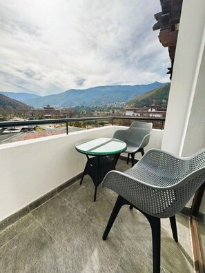 A balcony with a table and two chairs, overlooking a mountainous landscape with traditional buildings. - Dzi Apartments (Thimphu)