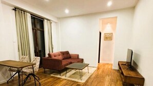 Un salon avec un plancher en bois, un canapé rouge, une table basse, un meuble pour la télévision et une table à manger.
